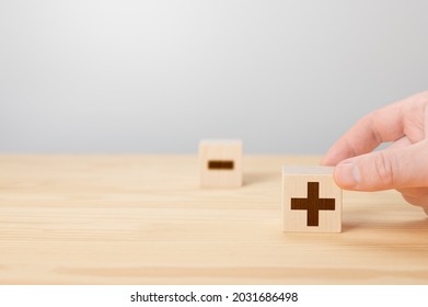 Person Holding Plus Sign Block Against Minus. Plus or minus. man hold cube with plus icon. hand choose wood cube with plus sign. blurred wooden cube with minus icon. Copy space