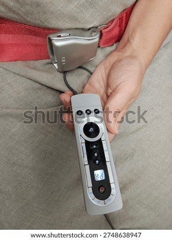 Person is holding a remote control with a timer on it. The remote control is on a grey surface in airplane