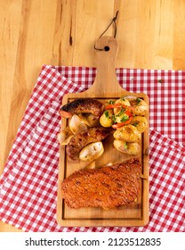 Person Holding A Slices Of Roast Beef With His Hand And Cooking Tongs Accompanied By A Portion Of Guacamole And Chirmol The Tomatoes,  Small Seasoned Potatoes On A Red Plain Blanket And Wood Board 