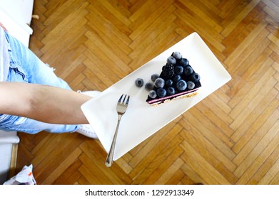 A Person Is Holding Square Plate With Piece Of Blueberry Cake On It 