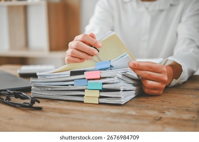 A person is holding a stack of papers on a desk. The papers are organized with colorful sticky notes. The person appears to be focused on the papers, possibly reviewing or sorting through them
