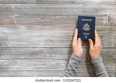 Person Holding A US Passport On A Wooden Desk From Above