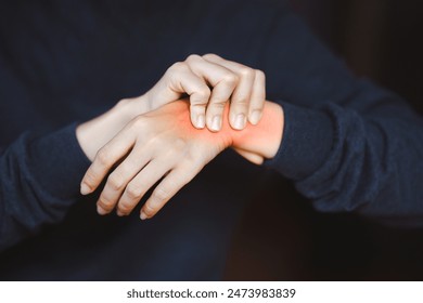 Person holding wrist with visible pain or inflammation, indicating injury or discomfort, on a dark background. Concept of pain or health issues. - Powered by Shutterstock