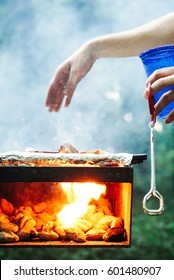 Person Holds A Blue Solo Cup As They Stoke A Roaring, Fiery Charcoal Grill In Preparation For A Dinner Party.