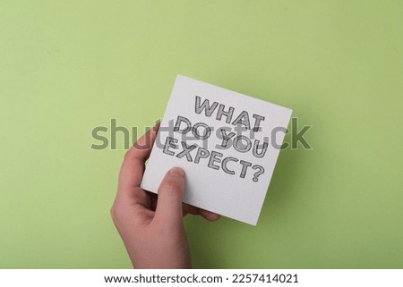 Person holds card with text What Do You Expect on light green background upper view. Anticipation and implementation of ideas in business industry
