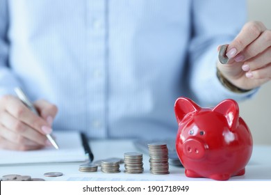 Person holds coins over piggy bank and makes notes in documents. Profitable deposits in banks concept