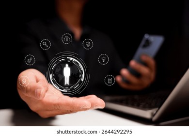 A person holds a holographic digital interface displaying a human icon surrounded by various technology and network symbols above an open laptop. - Powered by Shutterstock - Get 15% off with code: PIKWIZARD15