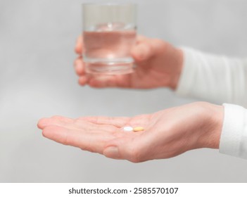 Una persona sostiene una píldora en una mano mientras busca un vaso de agua con la otra, lo que indica un momento de ingesta de medicamentos.