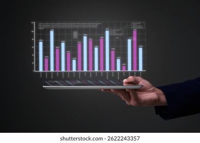 A person holds a tablet projecting a colorful, futuristic bar chart hologram with business data visualizations.