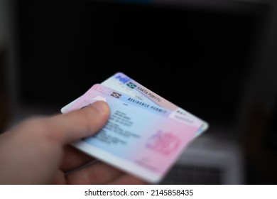 Person holds UK Residence Permit - BRP card and Poland Residence card (Karta Pobytu)  in hand and computer in the background. Immigration concept image. - Shutterstock ID 2145858435