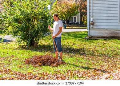 Person homeowner man in garden yard backyard raking dry autumn foliage oak leaves pile standing with rake in fall sunny sunlight by house - Powered by Shutterstock