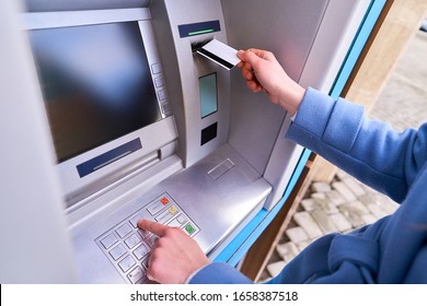 Person insert plastic credit card into atm bank and dials a PIN code on the keyboard to withdrawing money  - Shutterstock ID 1658387518