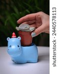 A person inserts money into a small blue hippo, with copy space available for personalization.