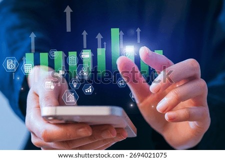 A person interacts with a smartphone displaying data graphs and icons in a contemporary office setting. The scene illustrates business analytics and technology usage.