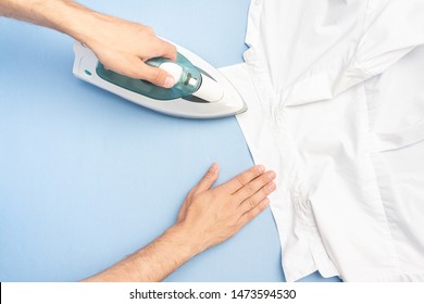 Person ironing his shirt, men's hands with iron, closeup, top view, close up