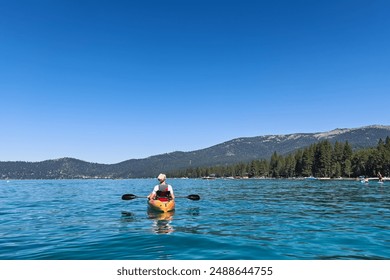 Person kayaking on a calm, clear blue lake with mountains in the background on a sunny day. - Powered by Shutterstock