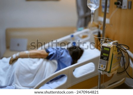 A person lies in a hospital bed connected to an IV drip.