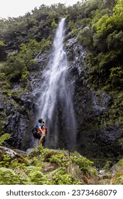 Person located at the foot of a waterfall and looking towards it. Route that runs from the road between the levada of Caldeirão Verde and Caldeirão do Inferno