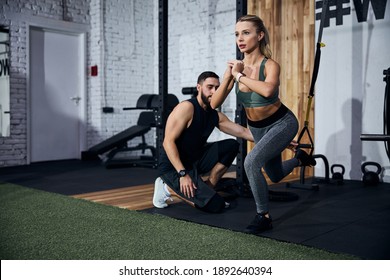 Person locking her hands together while doing a single-leg squat with an instructor placing her leg in a strap loop - Powered by Shutterstock