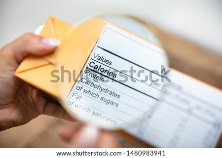 A Person Looking Nutrition Facts On Package Through Magnifying Glass
