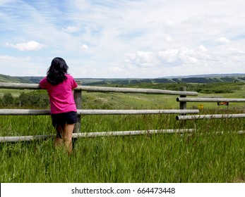 Person looking out over the wood fence at the prairie grasslands of the ranch