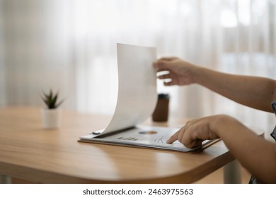 A person is looking at a piece of paper on a table. The paper is open to a page with a graph on it. The person is pointing at the graph with their finger - Powered by Shutterstock