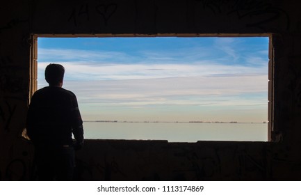 Person Looking Through The Window At The Landscape. It Is The Mar Menor. In The Background You Can See La Manga