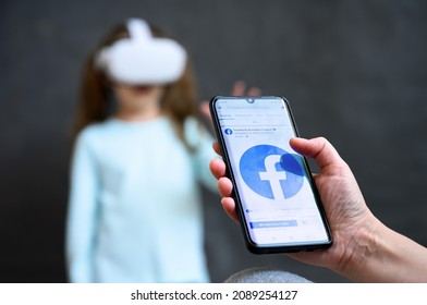 Person Looks At Facebook Social Media In Mobile Phone On Background Of Kid Using Futuristic Virtual Reality Headset. Concept Of Meta VR Technology, Metaverse And Video Games. Moscow - Dec 2, 2021