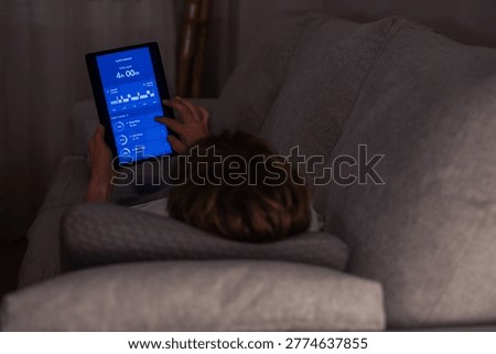 Person lying in bed and using a digital tablet to view sleep tracking results, showing a short duration of sleep and indicators of insufficient rest and exhaustion