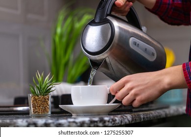 A Person Makes Tea Using Boiling Water From An Electric Kettle In Kitchen At Home. Time For Breakfast