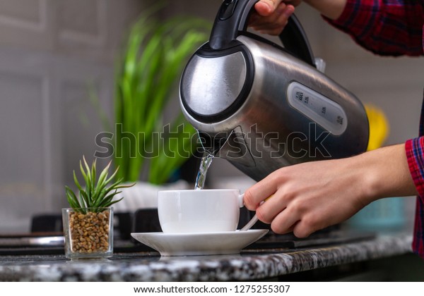 A person makes tea\
using boiling water from an electric kettle in kitchen at home.\
Time for breakfast