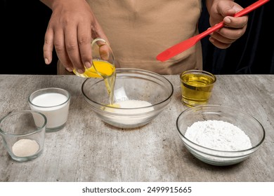 A person is making a dessert with a glass bowl containing eggs and a glass bowl containing flour. There are other bowls on the table with other ingredients - Powered by Shutterstock