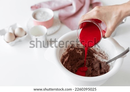 person making red velvet cake and adding red food coloring to batter. kitchen table with ingredients. cooking class concept. copy space