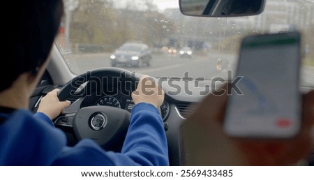 A person is maneuvering a car while simultaneously holding a cell phone in their hand, which can be quite risky while driving