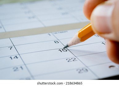 Person marking the date of the 15th with a pencil on a blank calendar with date squares as a reminder of an important day or to schedule a meeting or event