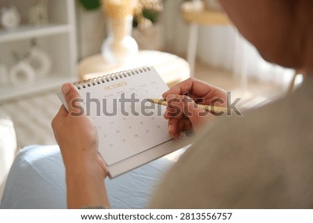 A person marks important dates on a calendar while seated indoors.