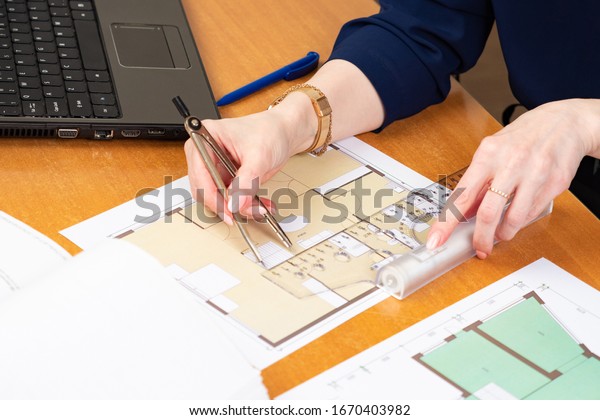 A person\
measures the size of the room according to the drawings. Architect\
with a ruler in his hands. Concept - approval of building drawings.\
Woman\'s hands with dividers and\
ruler.