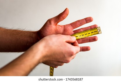 Person Measuring The Middle Finger Of His Left Hand With A Yellow Tape Measure. White Background. Olive Skin Tone. 