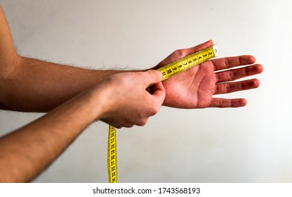 Person Measuring The Thumb Of His Left Hand With A Yellow Tape Measure. White Background. Olive Skin Tone. 