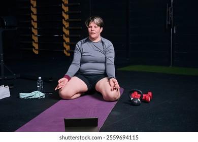 Person meditating on yoga mat in front of digital tablet in gym - Powered by Shutterstock