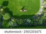 A person mows a well-maintained lawn, encircled by colorful plants and flowers in a residential yard.