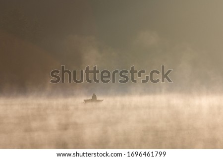 A person on a boat on the Spruce Knob Lake covered in the fog under the sunlight in West Virginia