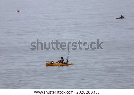 A person on a kayak with pedals and fishing gear out in the ocean in California.