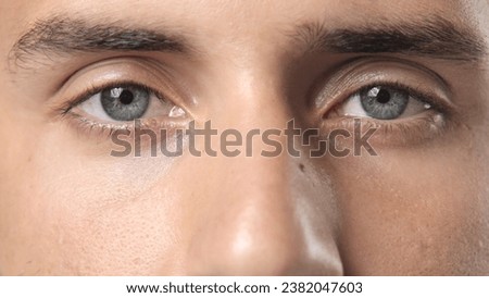 Person open beautiful blue eyes close up and look camera. Face portrait. 30s man opening eyelid. Eye sight gaze. Male model see clearly. Blue iris lens. Guy stare closeup