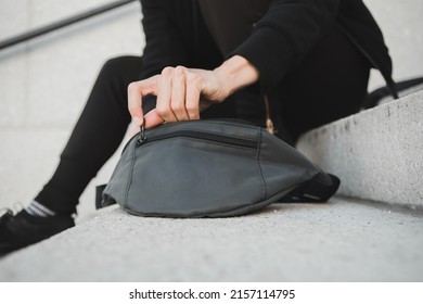 Person opening bum bag on the street wearing sporty clothing and sneakers