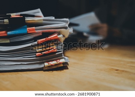 A person organizing a large stack of documents with binder clips on an office desk, representing paperwork, business management, and corporate workload.