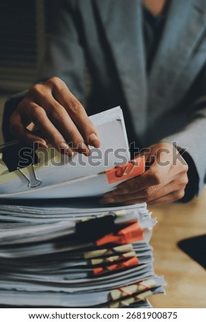 A person organizing a large stack of documents with binder clips on an office desk, representing paperwork, business management, and corporate workload.