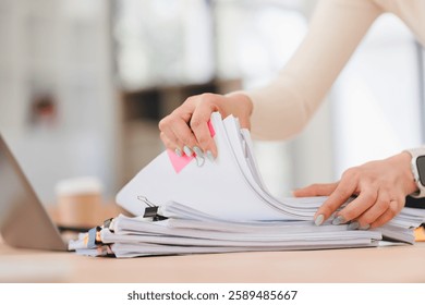 Person organizing stack of documents on desk, with laptop and coffee cup in background.