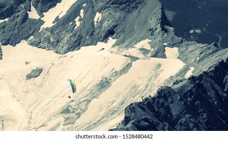 Person Paragliding From The Top Of Zugspitze Mountain With Jagged Cliffs In Background