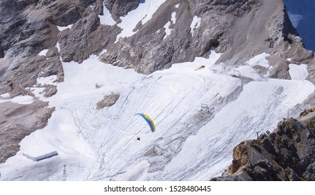 Person Paragliding From The Top Of Zugspitze Mountain With Jagged Cliffs In Background